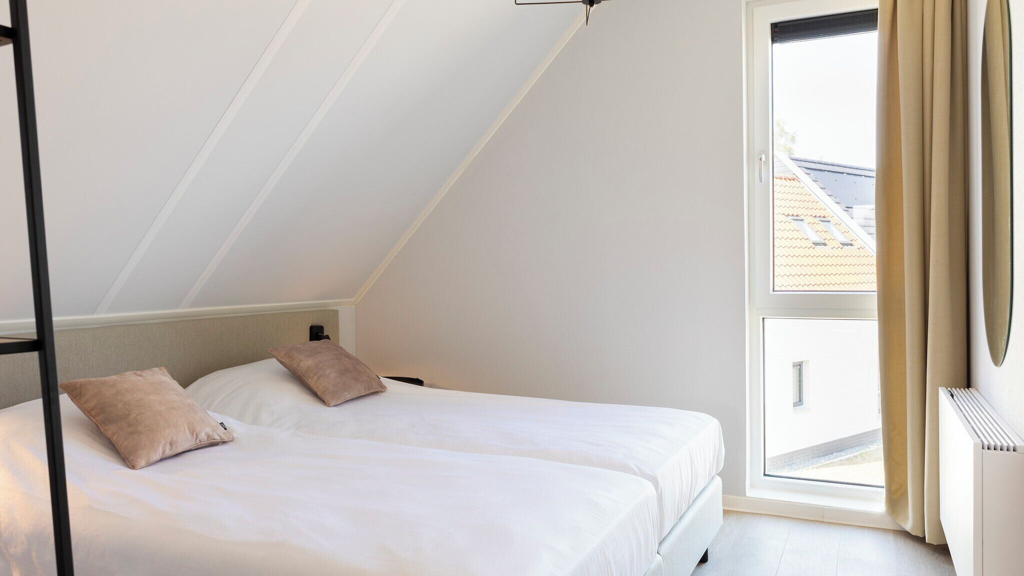 Une chambre avec deux lits, un plafond en pente et une grande fenêtre avec des rideaux.