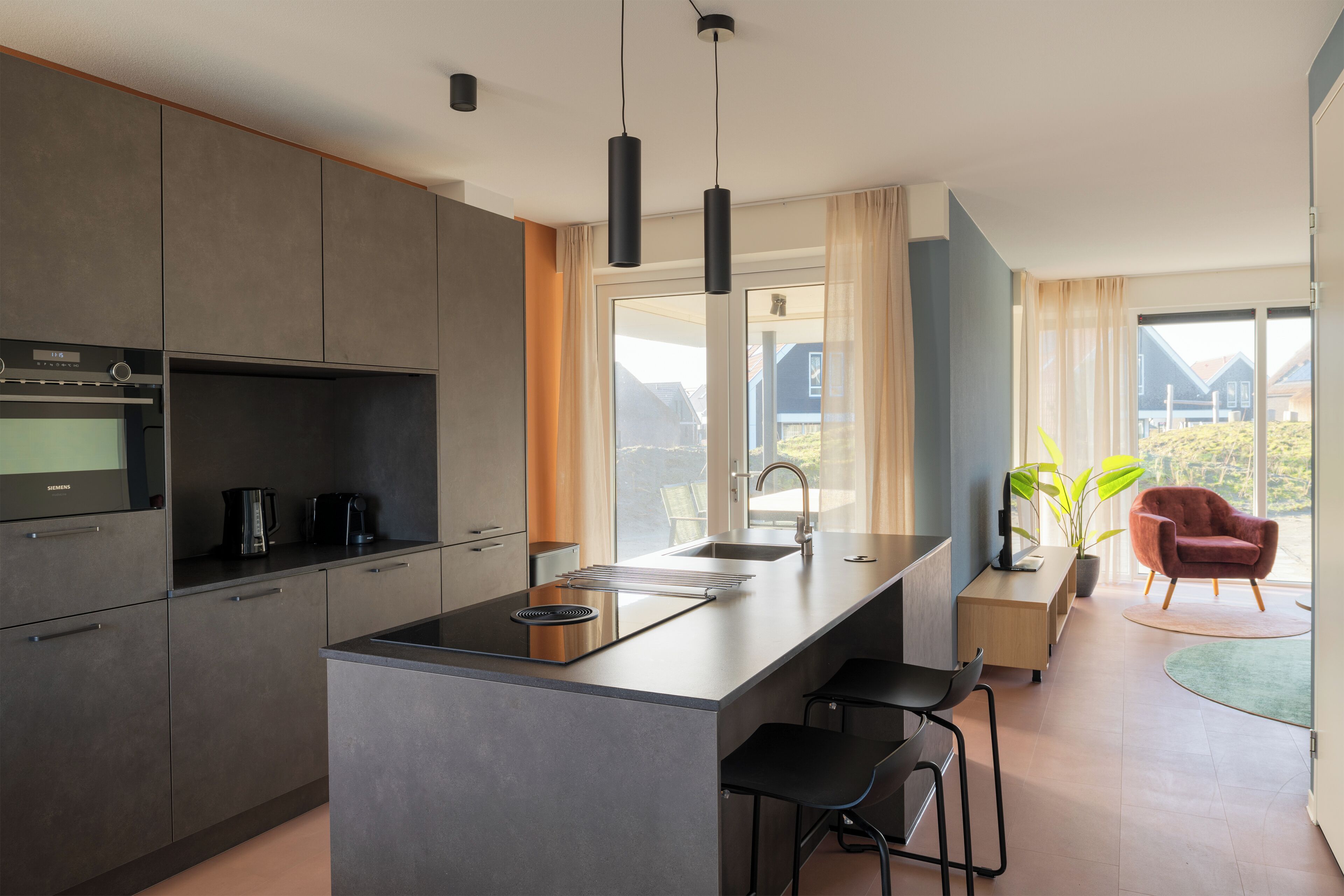Une cuisine moderne dotée d’un îlot central, d’appareils électroménagers en acier inoxydable et d’une grande fenêtre offrant une vue sur l’extérieur.