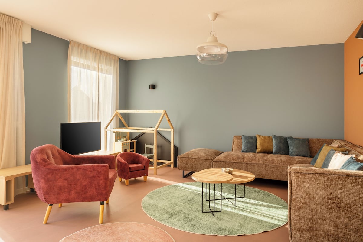 Una sala de estar con sofá, sillones, televisor, estructura de juego de madera y una escalera.