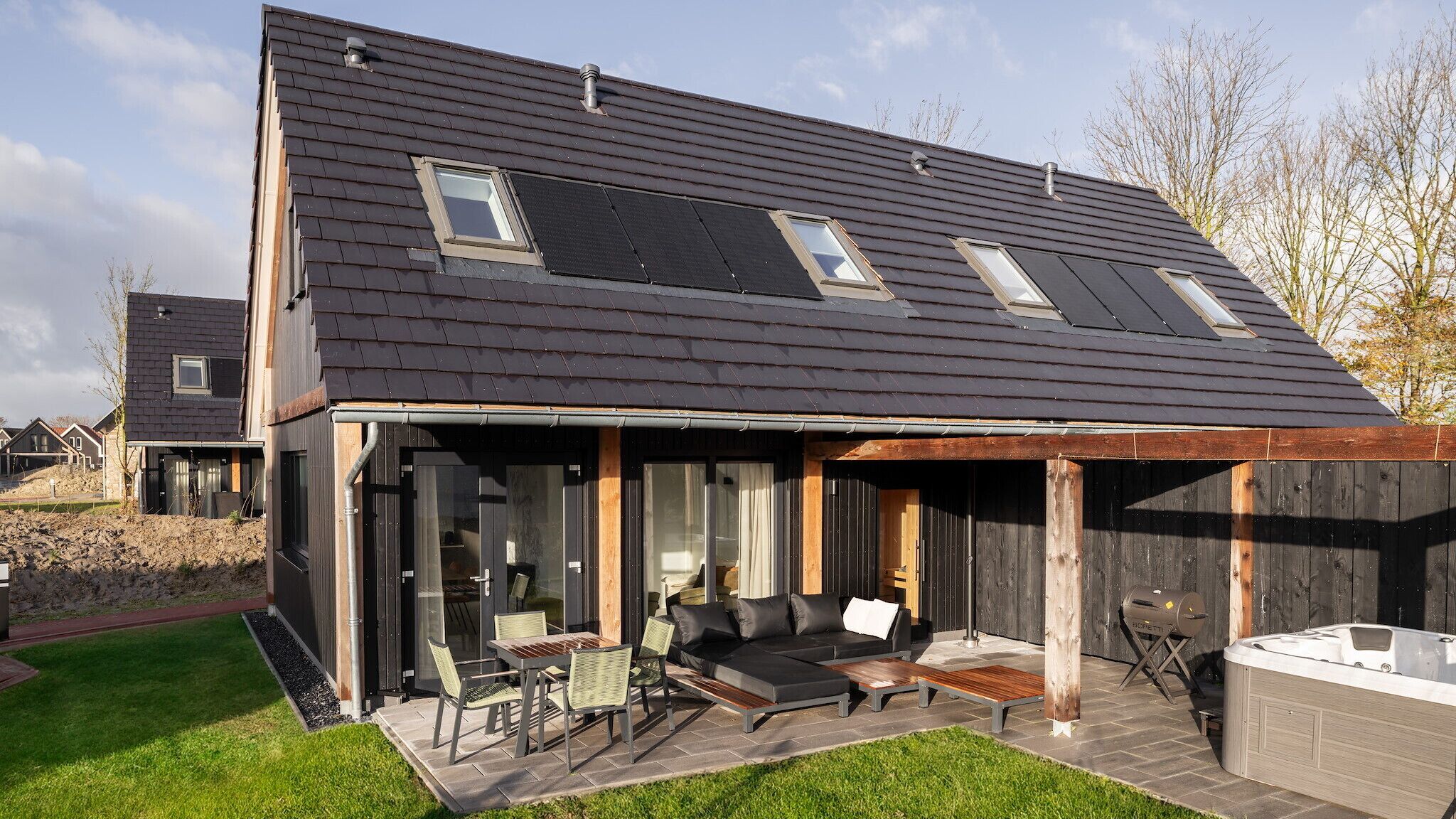 Une maison moderne dotée d’un toit en pente, de grandes fenêtres et d’un patio aménagé avec du mobilier d’extérieur.