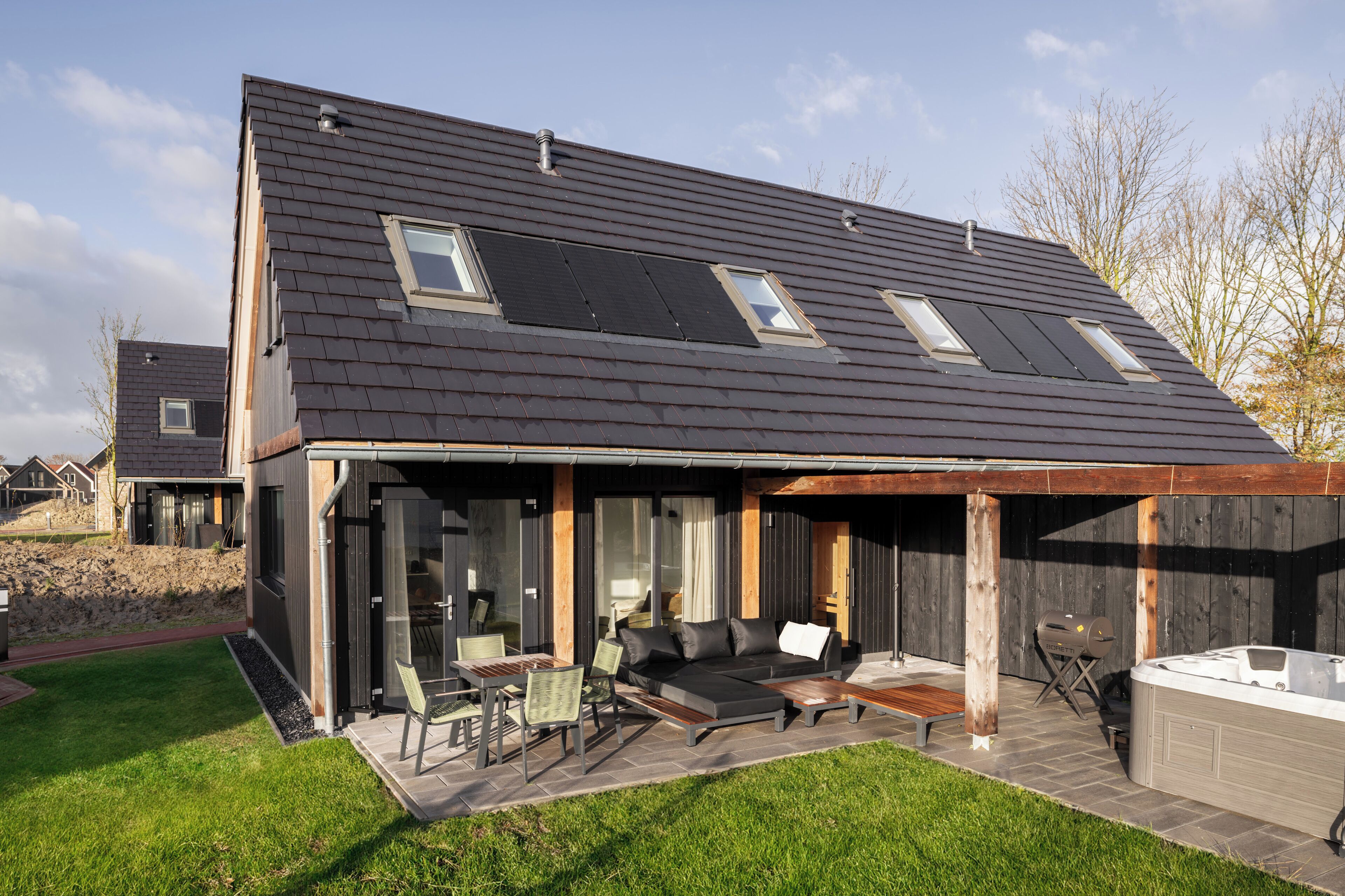A modern house with a sloped roof, solar panels, a patio with outdoor furniture, and a hot tub.