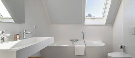 A modern bathroom with a freestanding bathtub, a toilet, and a vanity with a mirror.