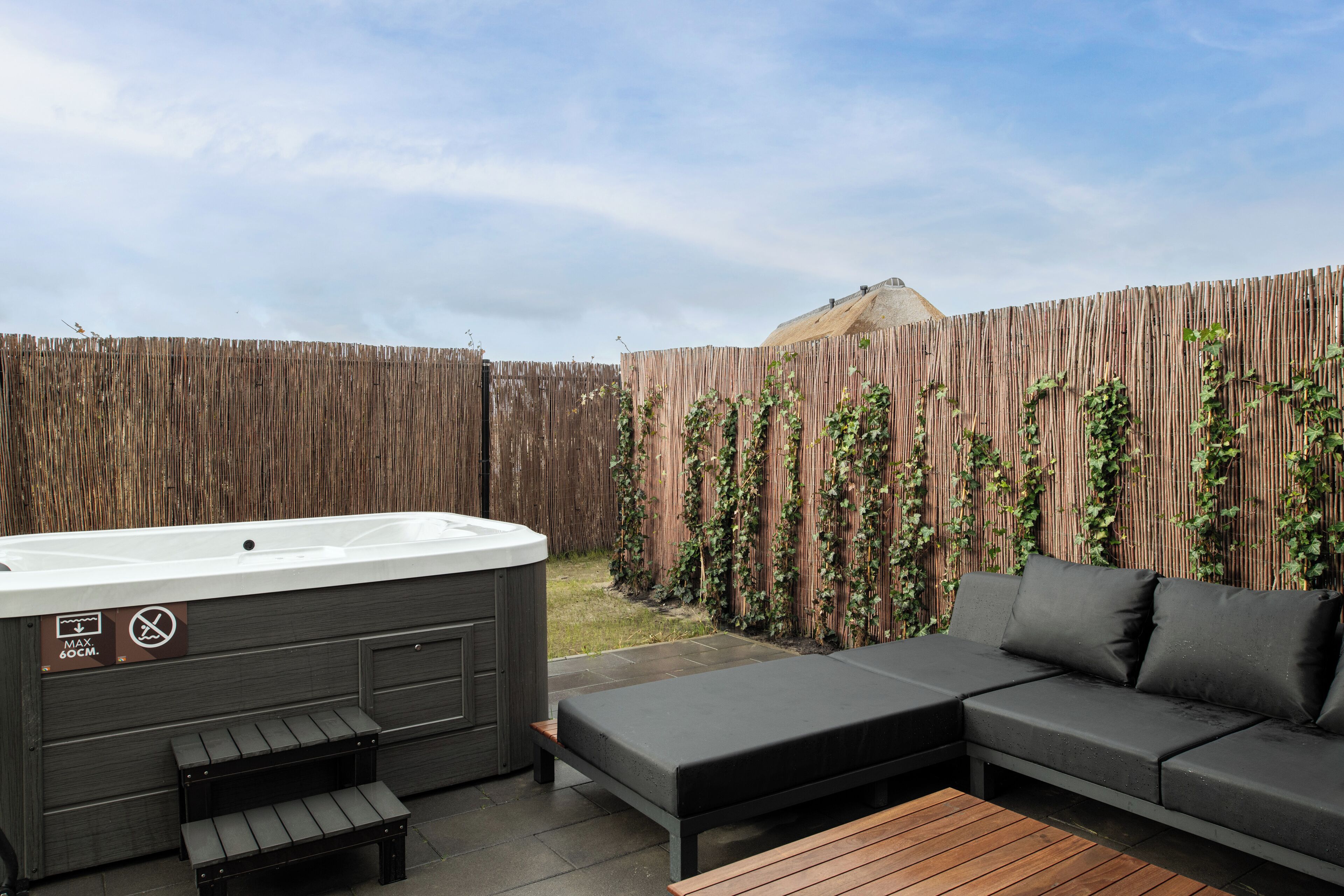 A hot tub, a sofa, and a wooden table in an outdoor patio area.