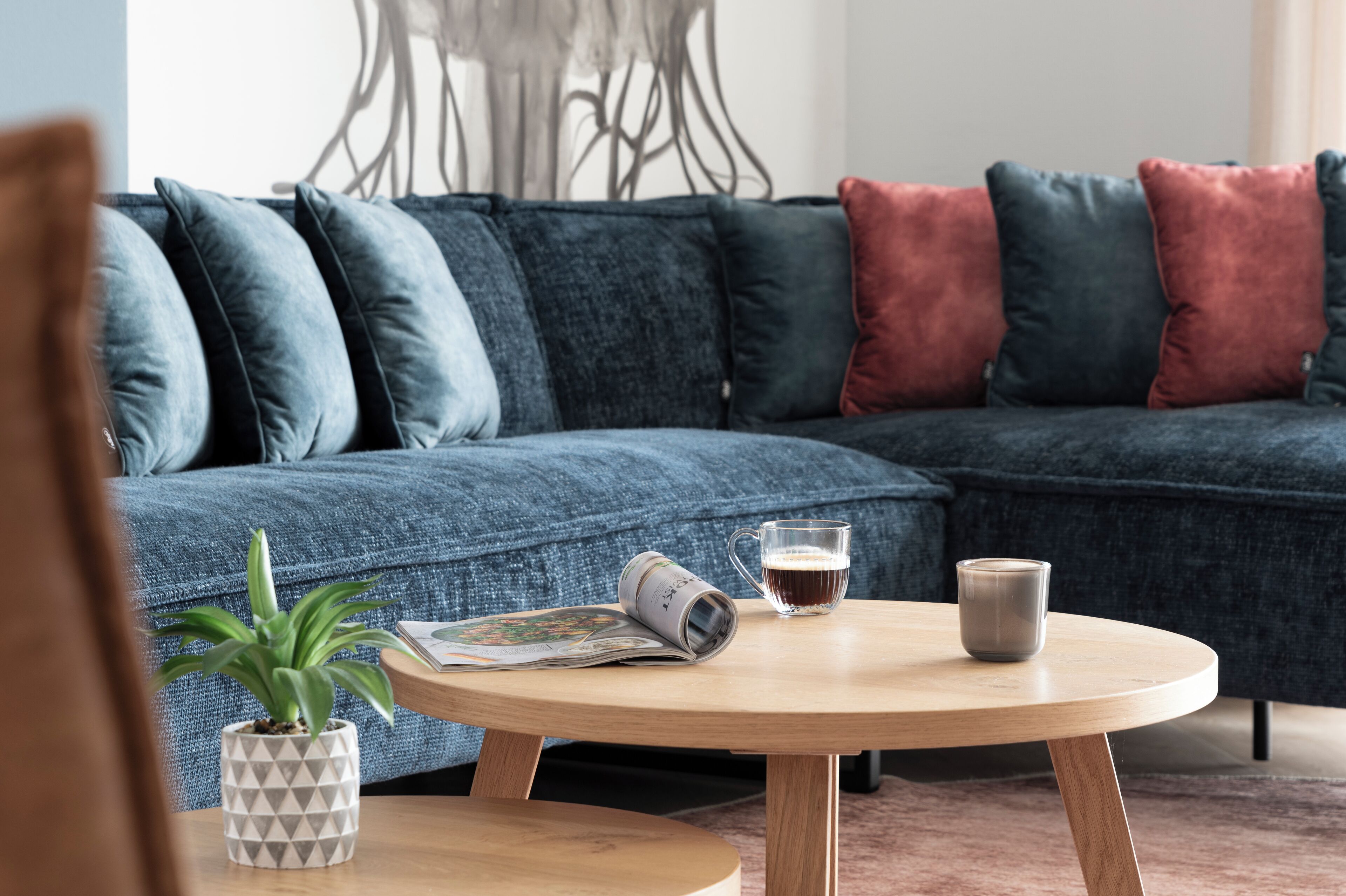 Un salon moderne avec un canapé bleu foncé, une table basse ronde en bois, une plante en pot et un magazine.