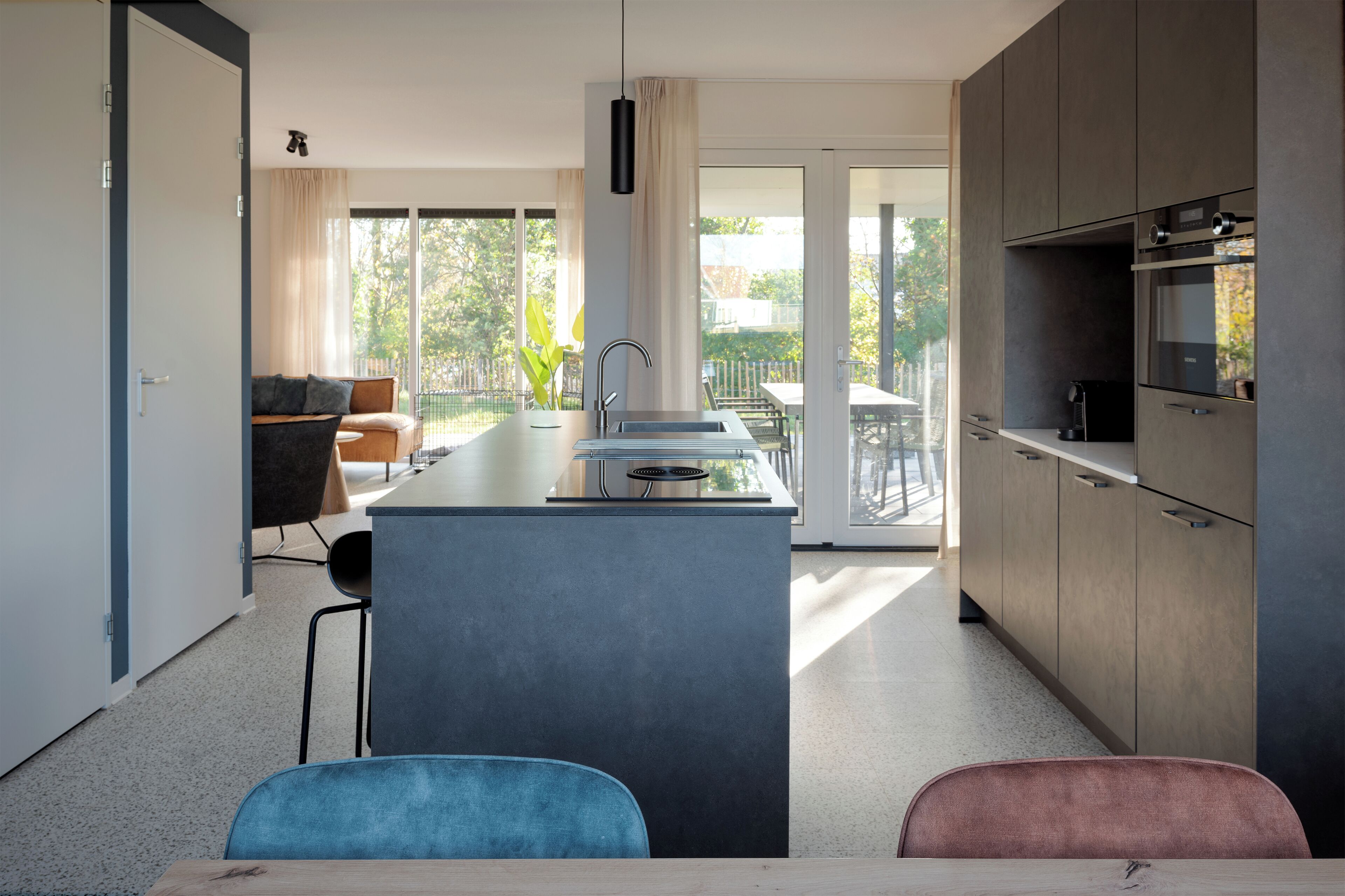 Una cocina moderna con una isla central, un comedor con sillas y vistas al exterior.
