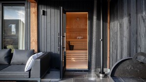 A modern outdoor sauna with a wooden interior, a black metal door, and a stone floor. - Dormio resort Nieuwvliet-Bad (Nieuwvliet)