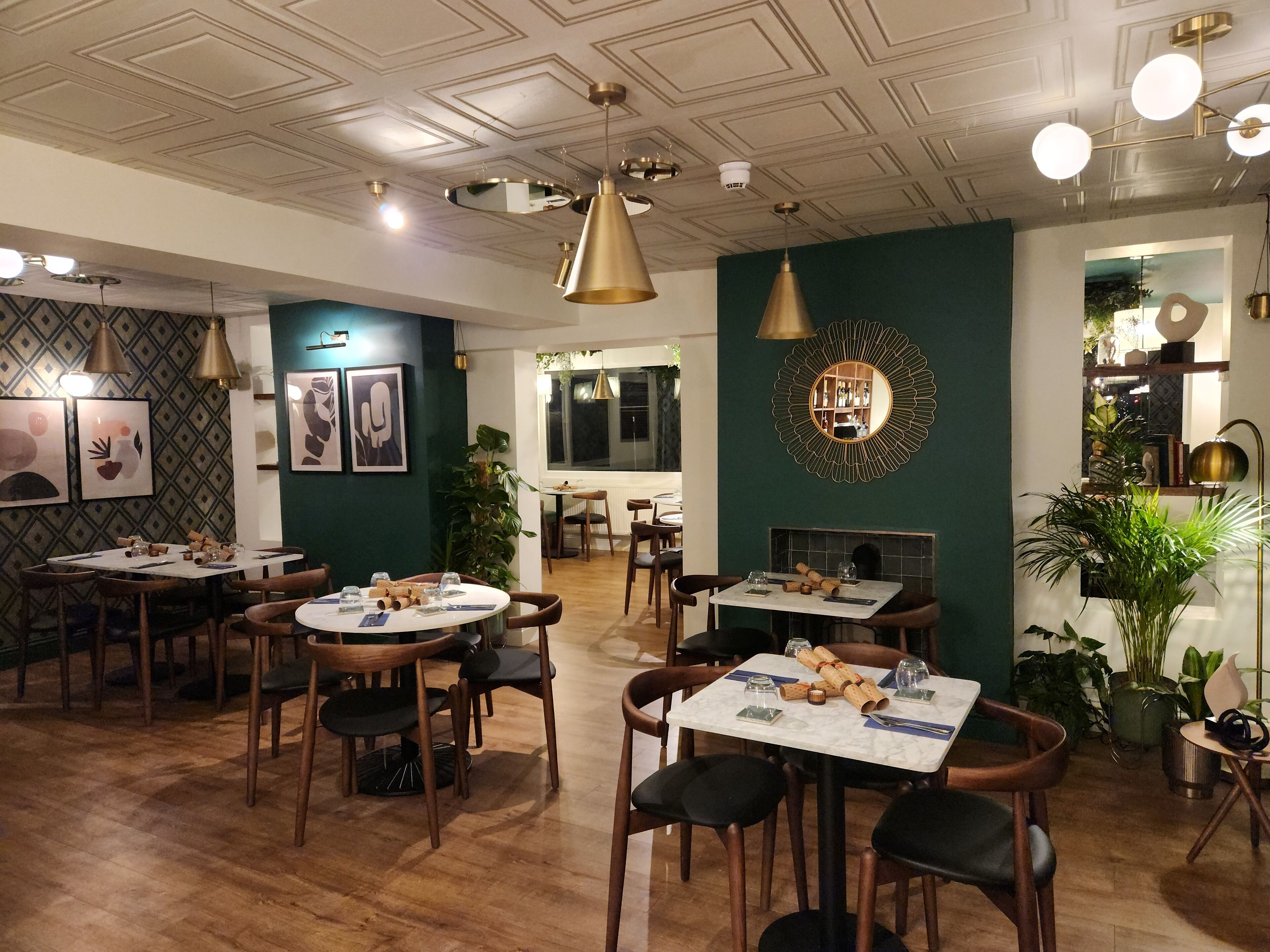 Un restaurant doté de nombreuses tables et chaises, d’un plafond décoratif et de miroirs fixés aux murs.