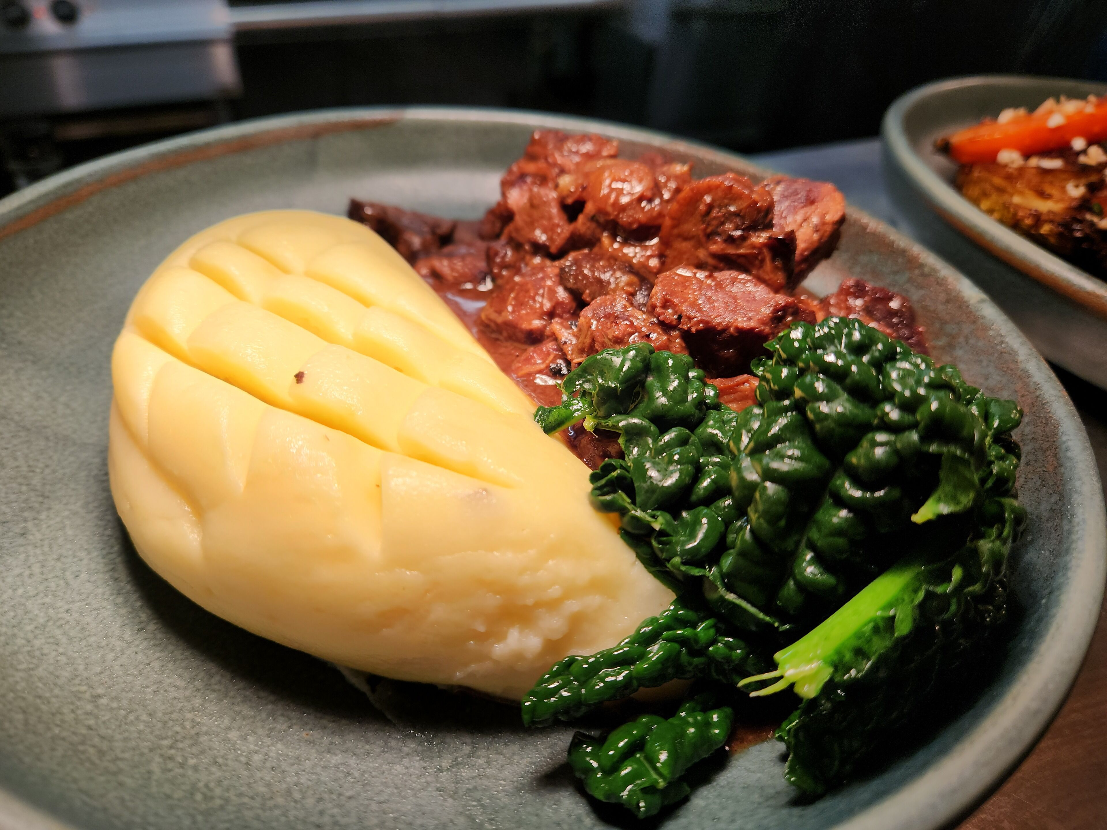 A plate with mashed potatoes, beef stew, and greens.