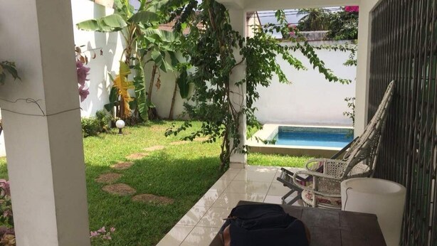 A patio with a pool, surrounded by greenery and a white wall. - Detached house with garden and indoor parking (Abidjan)