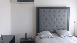 A bedroom with a large bed, a bedside table, a lamp, and a wall-mounted air conditioner. - Detached house with garden and indoor parking (Abidjan)