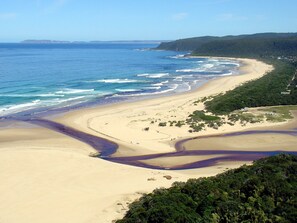 Un paisaje costero con playa arenosa, un canal serpenteante y una colina boscosa.