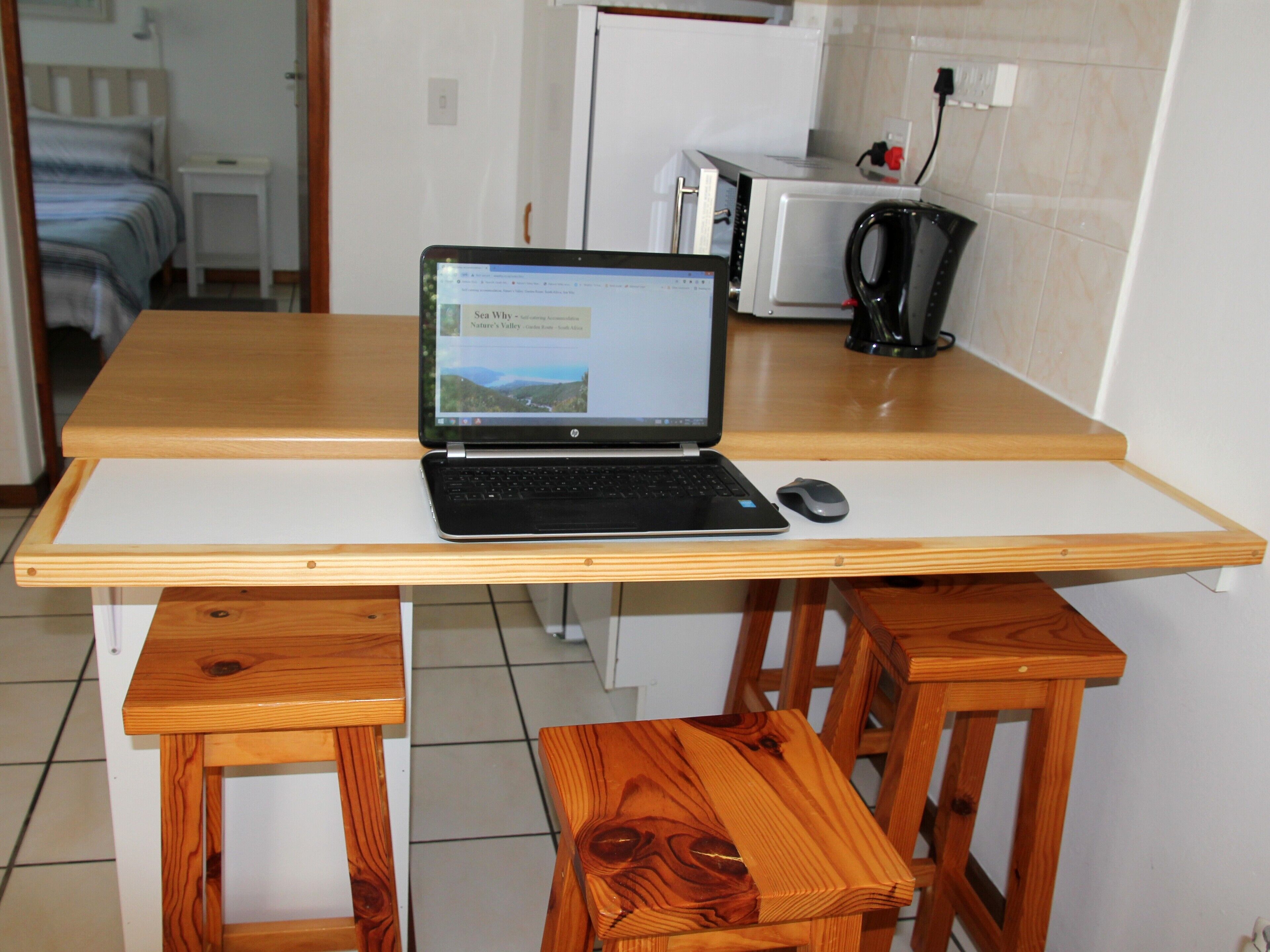 A laptop on a wooden table with a white surface, a black mouse, and a wooden chair.