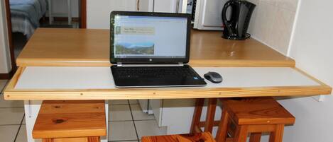 A laptop on a wooden table with a white surface, a black mouse, and a wooden chair.