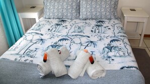 A neatly made bed with patterned bedding, a bedside table with a lamp, and a small nightstand with a phone. - Sea Why is a self-catering apartment in Nature's Valley , 5 min from the beach (Plettenberg Bay)