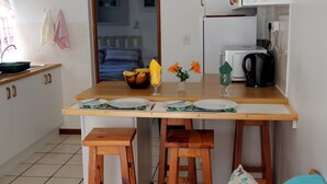A small kitchenette with a microwave, a kettle, and a fruit bowl on the counter. There are two stools and a table with plates and cutlery. - Sea Why is a self-catering apartment in Nature's Valley , 5 min from the beach (Plettenberg Bay)
