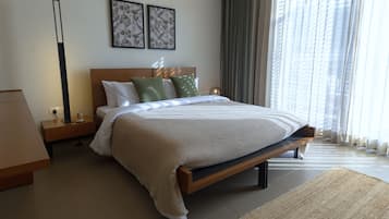 A modern bedroom with a large bed, a nightstand, a bedside table, a lamp, and two framed botanical prints on the wall.