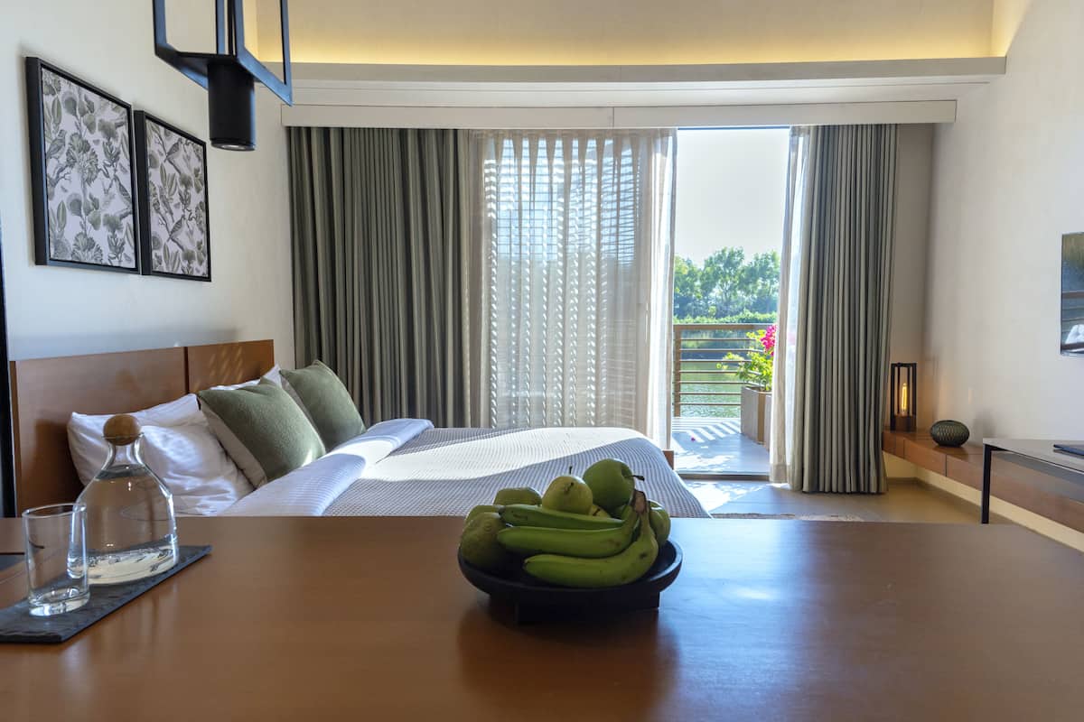 Habitación de hotel con cama, una mesa de comedor con frutero, una botella de agua y un vaso.