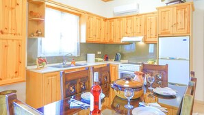 A kitchen with wooden cabinets, a stove, a sink, and a dining table set for two. - Galini Vines House Authentic Corfu Village Life Wifi A C (Corfu)