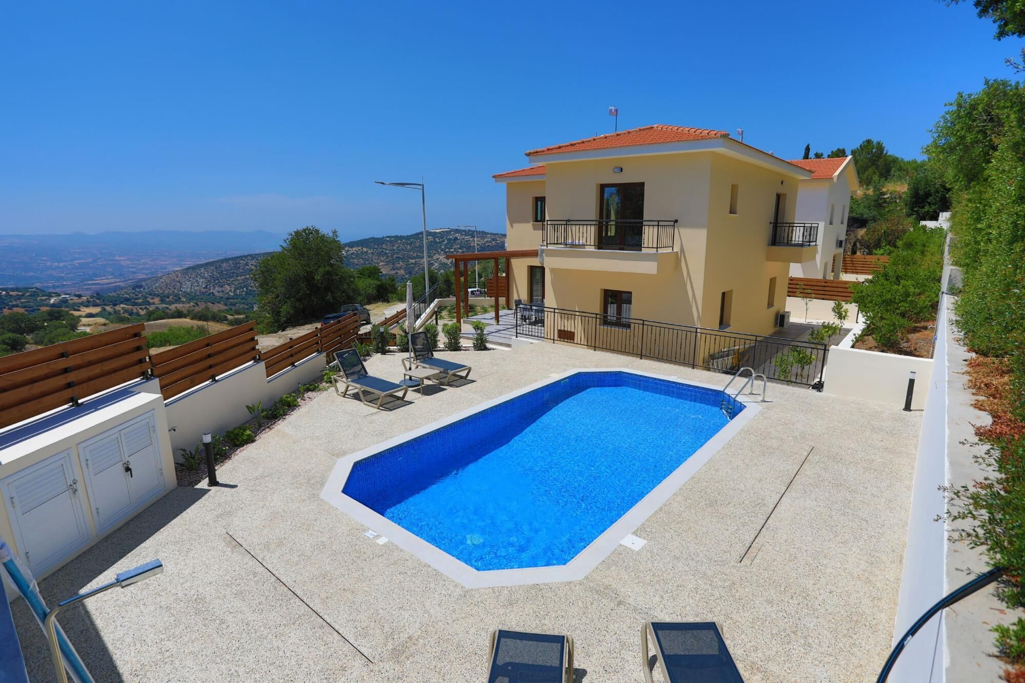 A two-story building with a swimming pool, outdoor seating, and a view of the landscape.