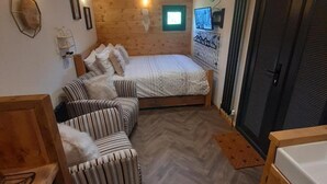 A cozy room with a bed, two striped sofas, a wooden floor, and a door.