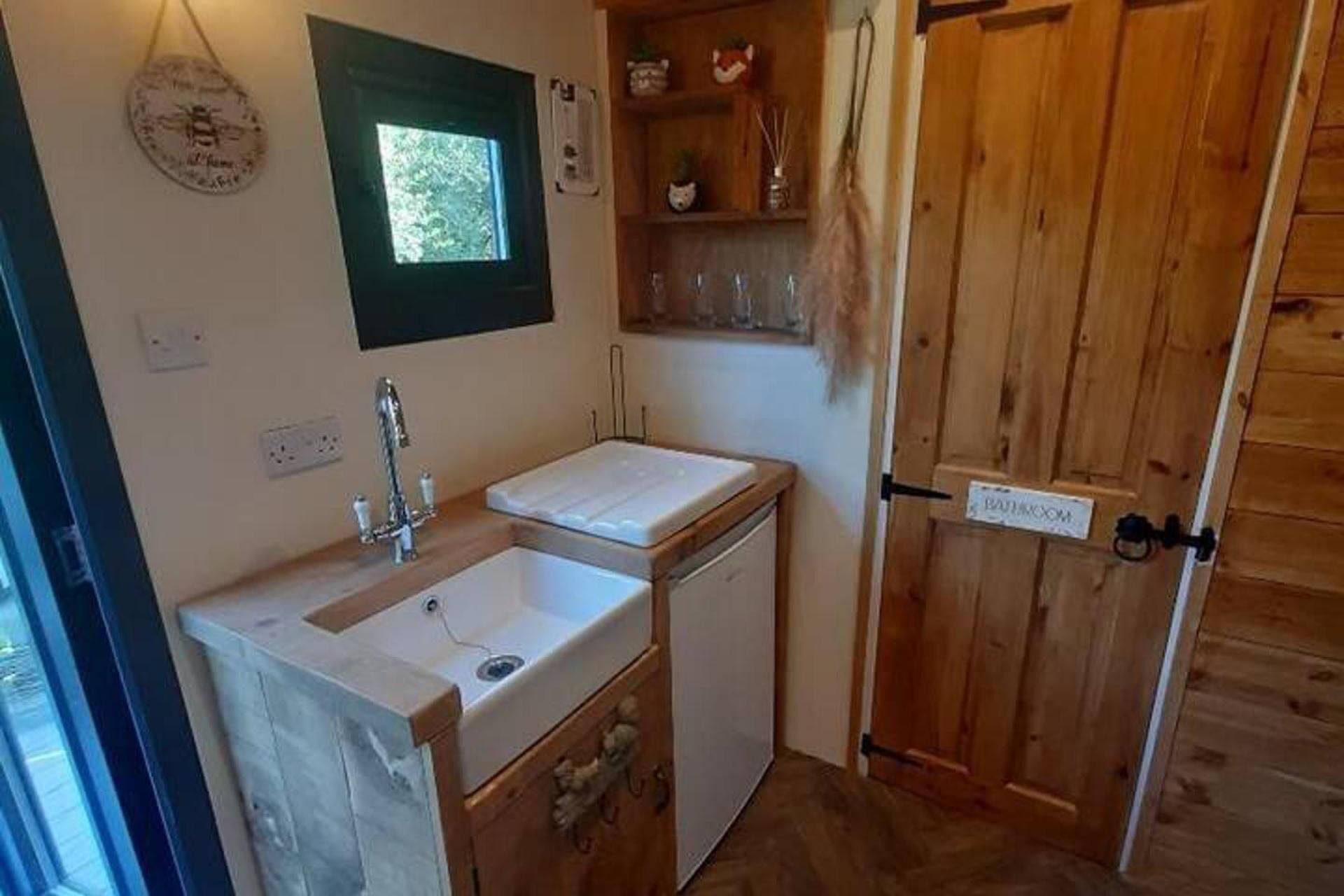 A compact kitchen with a sink, a small refrigerator, and a window above the sink.