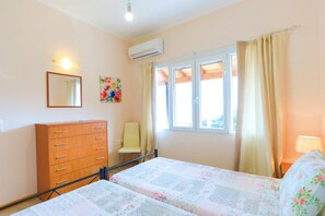 A bedroom with a bed, a wooden dresser, a chair, a window with curtains, and an air conditioning unit.