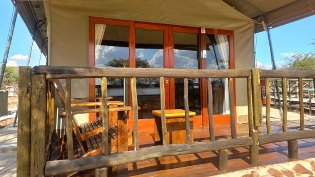 A covered outdoor area with a wooden deck, a table, and chairs. - Tsabong Eco-Tourism Camel Park (Tshabong)
