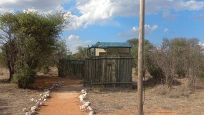 A rural setting with a dirt path leading to a wooden structure, a metal pole, and sparse vegetation. - Tsabong Eco-Tourism Camel Park (Tshabong)