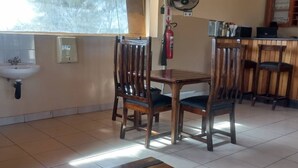 A dining area with a wooden table and chairs, a sink, and a fire extinguisher. - Tsabong Eco-Tourism Camel Park (Tshabong)