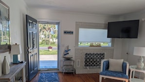 A living room with a blue sofa, a fireplace, a television, and a view of the outdoors. - Steps from the beach with pool! (Ormond Beach)