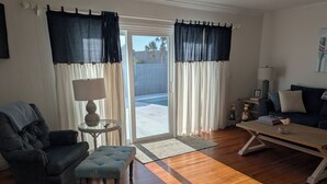 A living room with a dark blue sofa, a light blue ottoman, a wooden coffee table, and a lamp on a side table. - Steps from the beach with pool! (Ormond Beach)