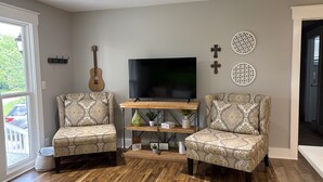 A living room with two patterned armchairs, a wooden coffee table, a television, decorative wall art, and a guitar. - Ivywood Escape Relaxing Stay (30+ Day Rental) (Nashville)