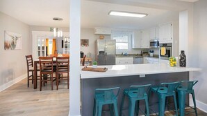 A modern kitchen with white cabinets, a central island with bar stools, and a dining area with wooden chairs. - Ivywood Escape Relaxing Stay (30+ Day Rental) (Nashville)