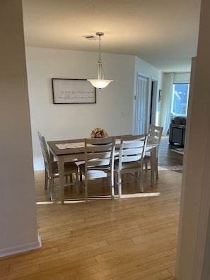 A dining area with a wooden table and chairs, a pendant light, and a framed quote on the wall.