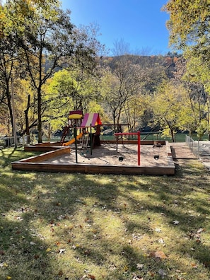 A playground with a slide and swings, surrounded by trees and a hilly landscape. - Awesome Pointe Royale Walk In (Branson)