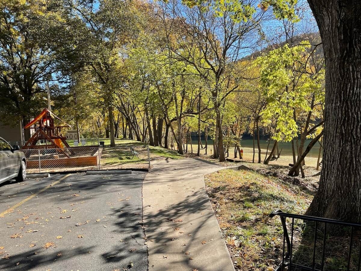 A paved pathway in a park with trees and a playground structure.