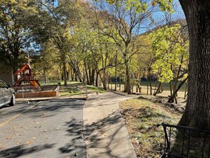 A paved pathway in a park with trees and a playground structure.