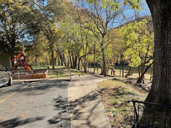 A paved pathway in a park with trees and a playground structure.