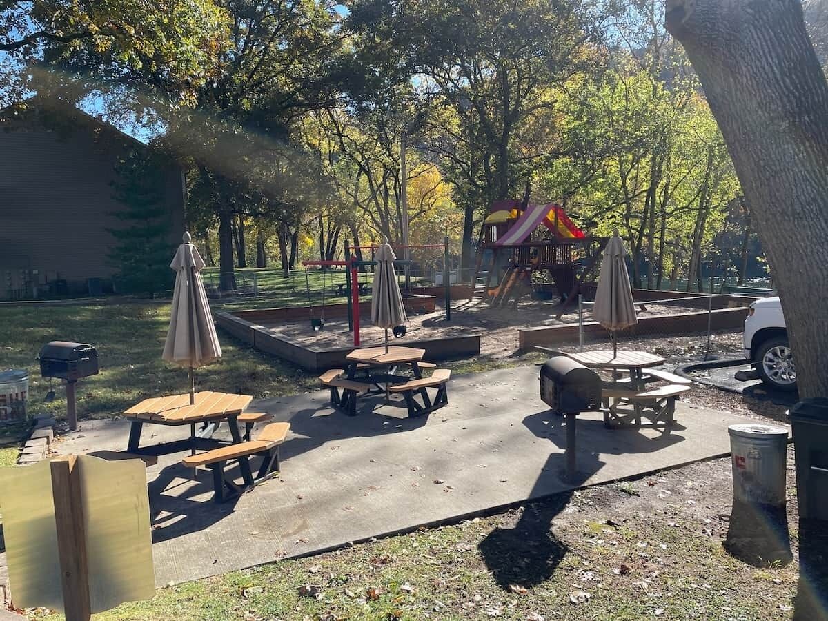 An outdoor park area with picnic tables, umbrellas, and a playground.