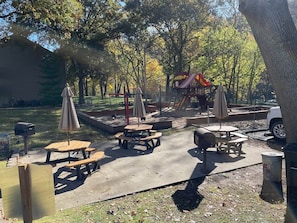An outdoor park area with picnic tables, umbrellas, and a playground.