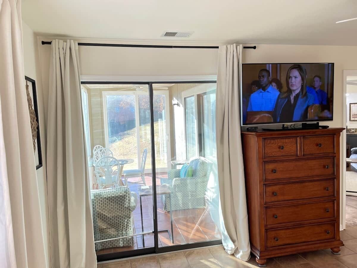A room with a sliding glass door leading to an outdoor seating area, a television on a stand, and a wooden dresser.