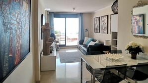 Een moderne woonkamer met een bank, eettafel en stoelen. Aan de muur hangt een groot schilderij en er is een raam met gordijnen.