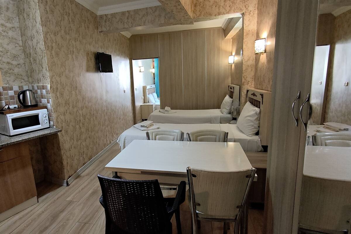 A compact hotel room with a kitchenette, a dining table, two beds, and a bathroom visible through an open door.