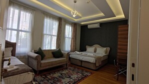 Ένα σύγχρονο υπνοδωμάτιο με έναν καναπέ, δύο κρεβάτια, ένα χαλί με σχέδια και ένα φωτιστικό οροφής.