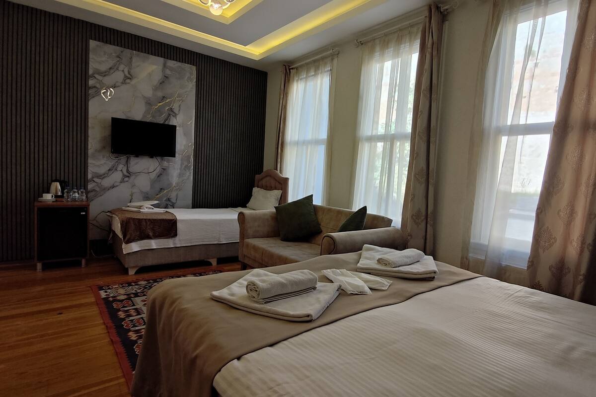 A modern hotel room with a large bed, a smaller bed, a sofa, and a TV mounted on the wall.