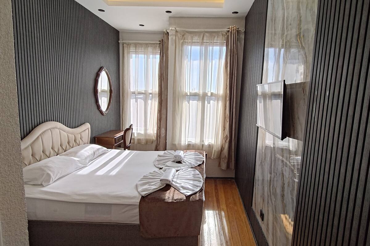 A hotel room with a large bed, a wooden nightstand, a mirror, and a TV mounted on the wall.