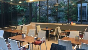 Ένας μοντέρνος χώρος τραπεζαρίας με μεγάλα παράθυρα, καρέκλες από μπαμπού και ξύλινα τραπέζια.