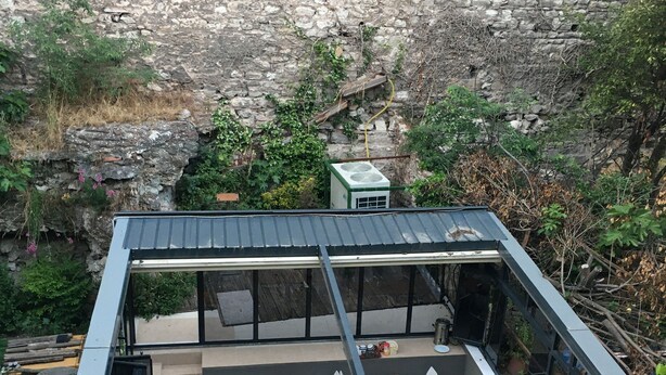 Ένας σύγχρονος, υπαίθριος χώρος για φαγητό, με τραπέζια και καρέκλες, που διαμορφώνεται με φόντο έναν τοίχο από πέτρα.