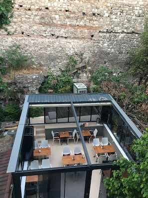 A modern outdoor dining area with tables and chairs, set against a stone wall backdrop. - Nuray Hotel (Istanbul)
