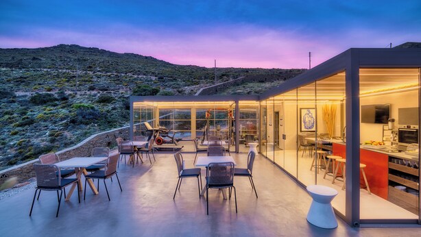 Un espace de restauration en plein air, doté de mobilier moderne et d’une cuisine fermée par des parois de verre.